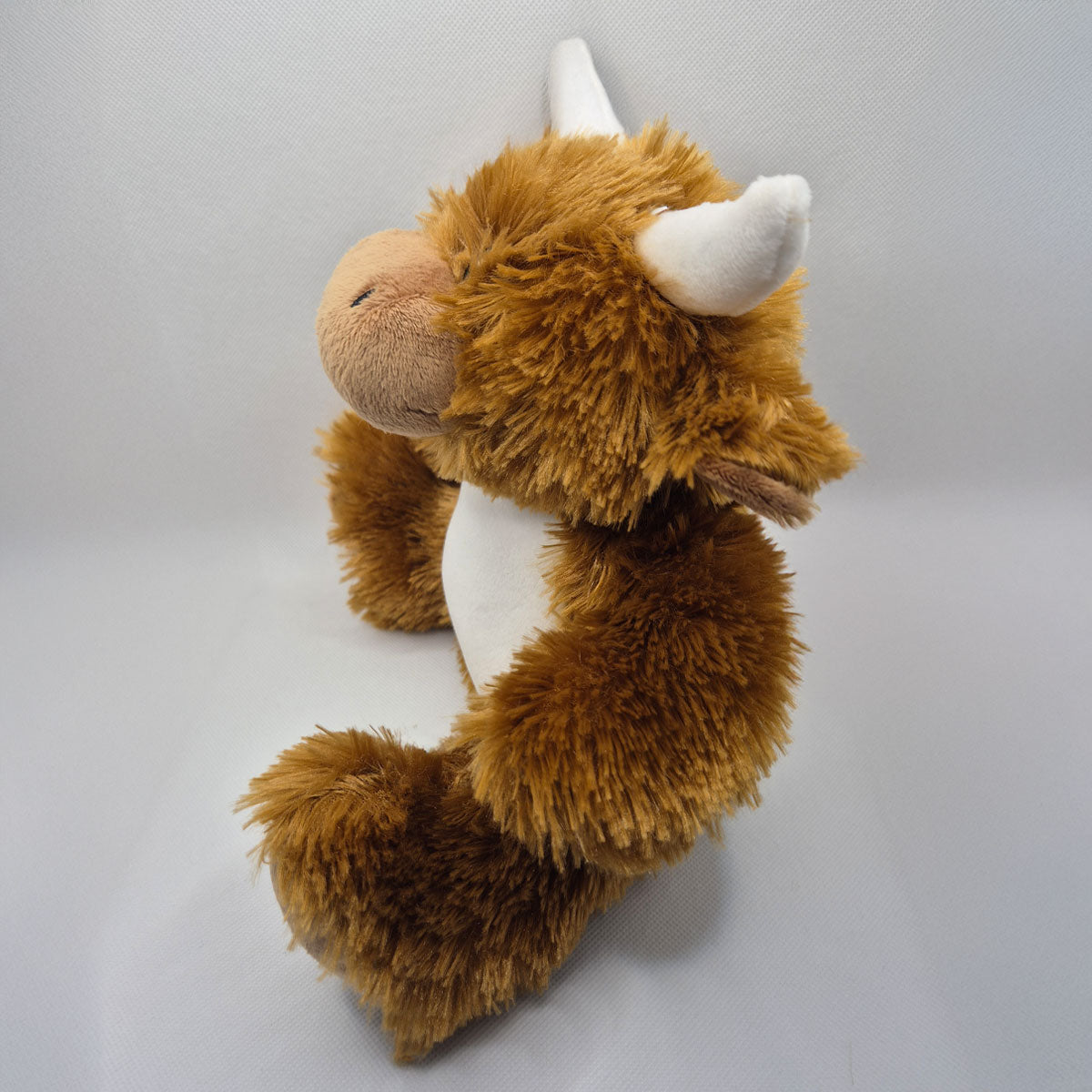 Plush highland cow teddy bear resembling with white horns on a gray background PHigh
