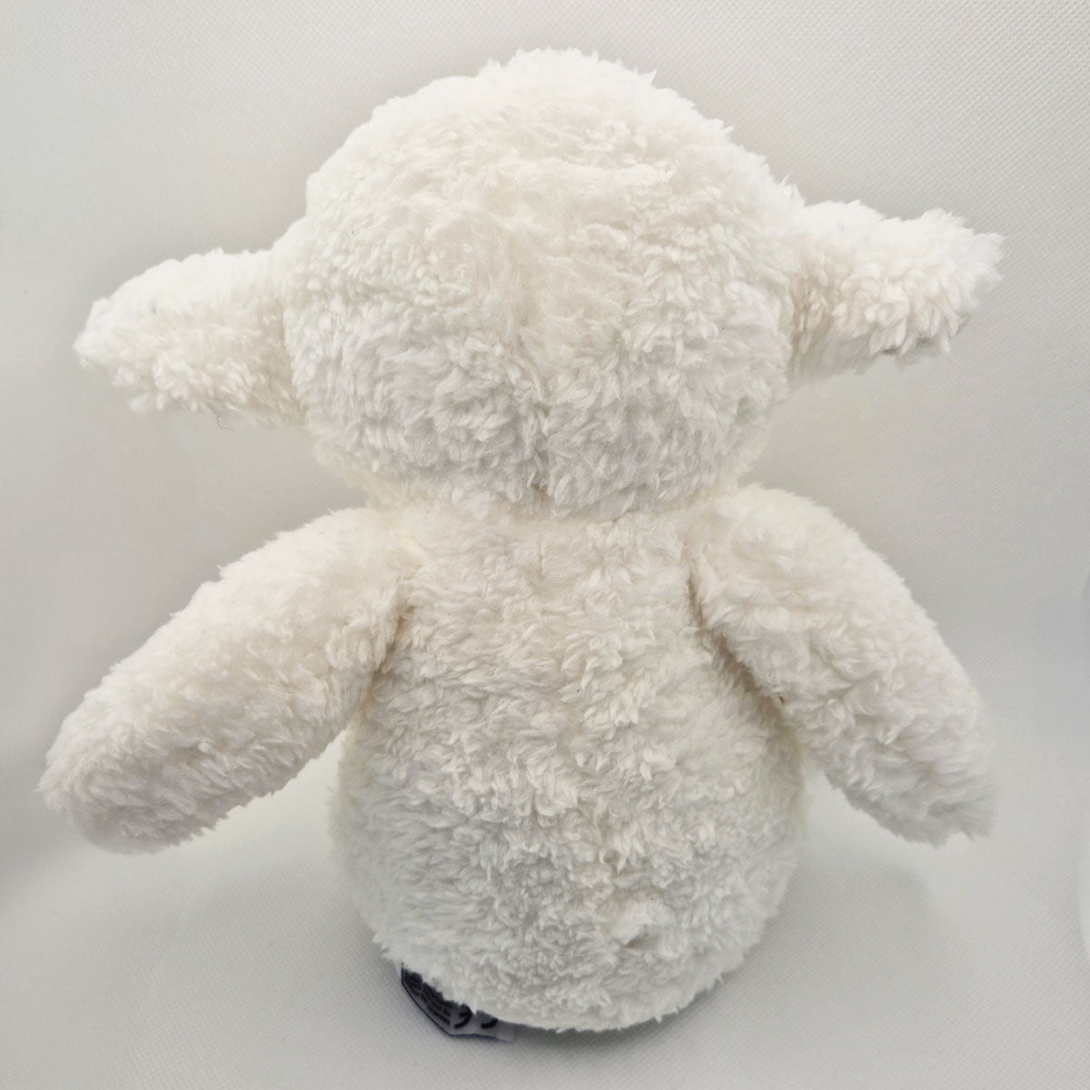 Back of a white lamb plush toy on a light gray background