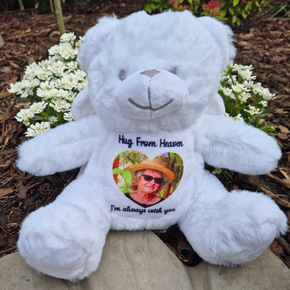White angel teddy bear with a heart-shaped photo and text on a stone surface with flowers in the background CFHANG