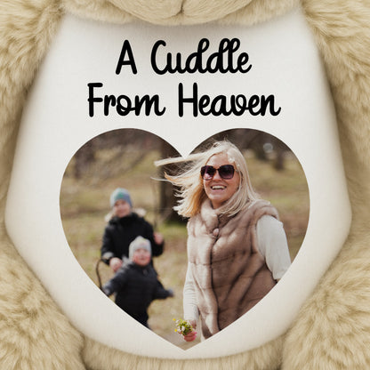 Teddy bear with printed Heart-shaped photo with a family picture and 'A Cuddle From Heaven' text, surrounded by fluffy beige fabric.