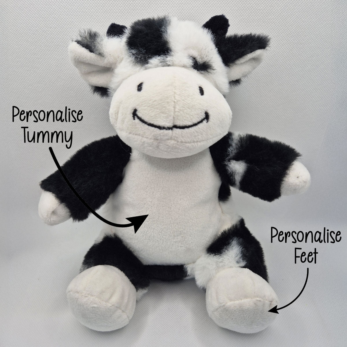 Plush cow teddy with text indicating areas to personalise on a light gray background