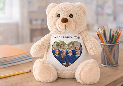 Brown teddy bear with a heart-shaped photo printed on it placed on a desk with stationery items.