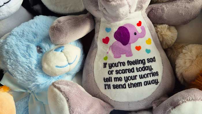 Plush toy with an elephant design and message surrounded by other plush toys.